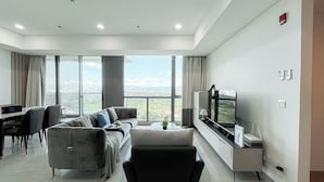 Una sala de estar moderna con un sofá, televisor y vista a la ciudad a través de amplios ventanales.
