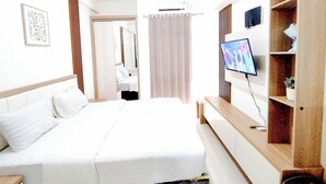 Een hotelkamer met een bed, een televisie, een bureau en een badkamer, zichtbaar door een geopende deur.