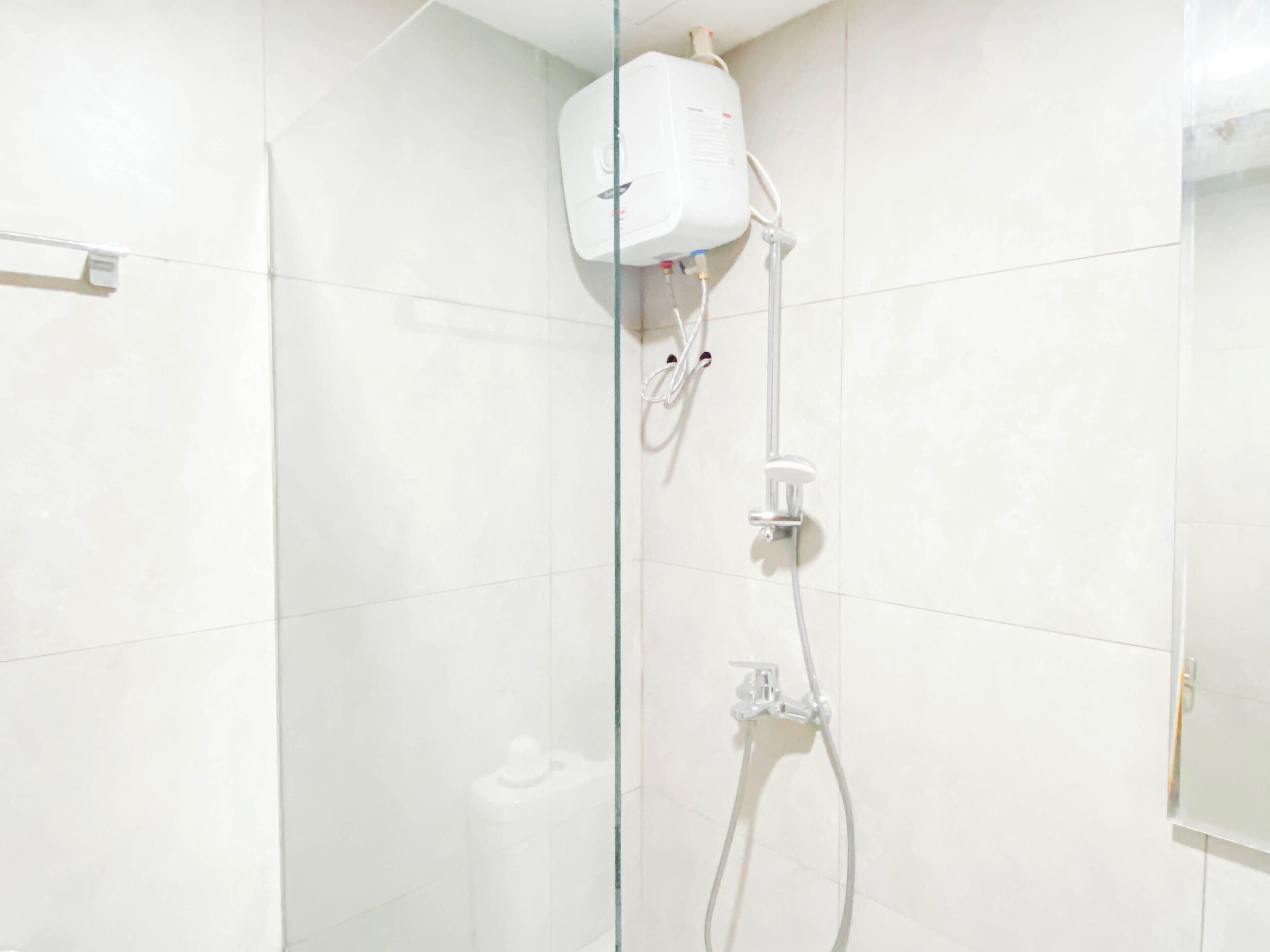 A modern bathroom with white tiles, a glass shower enclosure, and a white water heater mounted on the wall.