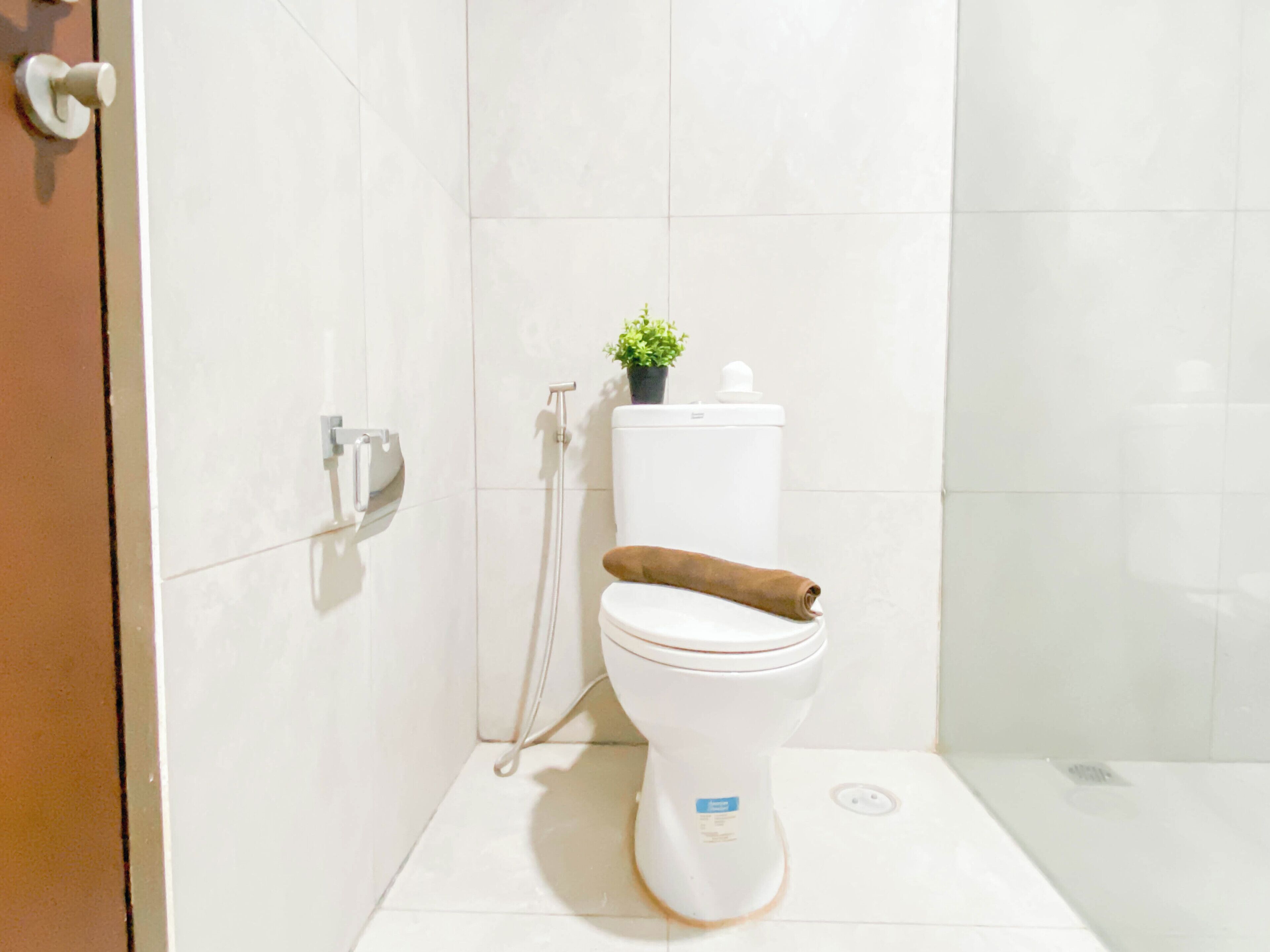 Une salle de bain avec des toilettes, une douche et une petite plante en pot posée sur le réservoir des toilettes.