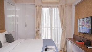 A hotel room with a bed, a desk with a TV, and a window with curtains.
