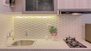 A kitchen with a stainless steel sink, a gas stove, and a window above the countertop. - Good Choice And Homey Studio Grand Kamala Lagoon Apartment (Bekasi)