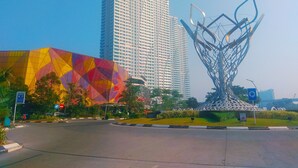 A modern building with a geometric glass facade and a unique metal sculpture in front. - Good Choice And Homey Studio Grand Kamala Lagoon Apartment (Bekasi)