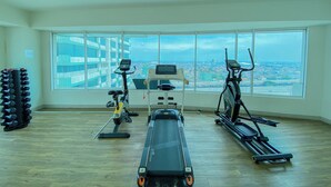A spacious gym with a rowing machine, elliptical, and treadmill, large windows with a city view. - Good Choice And Homey Studio Grand Kamala Lagoon Apartment (Bekasi)