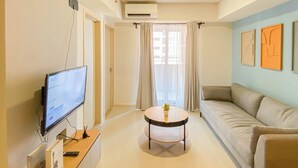 Una sala de estar moderna con un televisor de pantalla plana, una mesa de centro redonda, un sofá color beige y una ventana con cortinas traslúcidas.