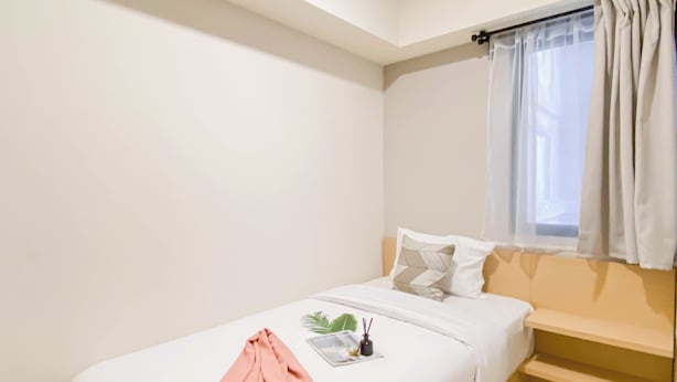 Un dormitorio pequeño y ordenado con una cama individual, una ventana con cortinas y una mesita con una planta y una botella.