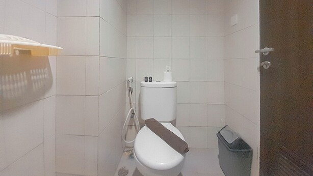 A small, white-tiled bathroom with a toilet, a trash bin, and a towel rack. - Comfortable And Homey 2Br Apartment At Mekarwangi Square Cibaduyut (Bandung)