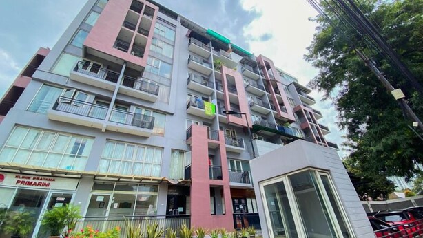 Un immeuble à plusieurs étages doté de balcons, une clinique nommée « Primarni » située au rez-de-chaussée, et un petit kiosque ou magasin également au rez-de-chaussée.