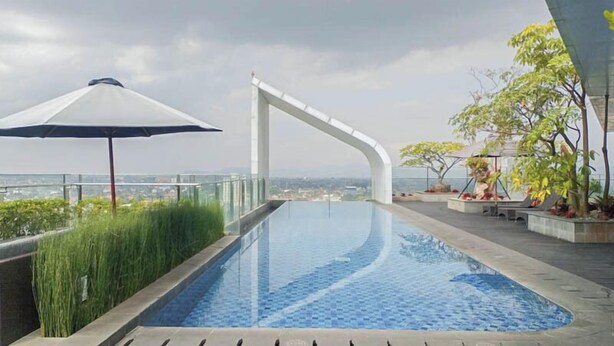 Una piscina infinita en la azotea con vistas despejadas del paisaje urbano, rodeada de vegetación y arquitectura moderna.