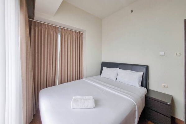 A neatly made bed with a folded towel, a dark headboard, and a small bedside table with a lamp.