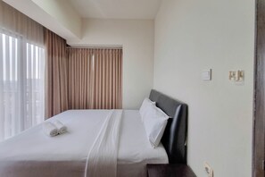 A hotel room with a neatly made bed, a headboard, and a window with curtains.