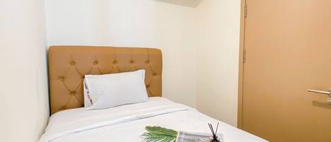 A neatly made bed with a white comforter, a pink blanket, and a white pillow. There is a tray with a plant, a bottle, and a glass container on the bed.