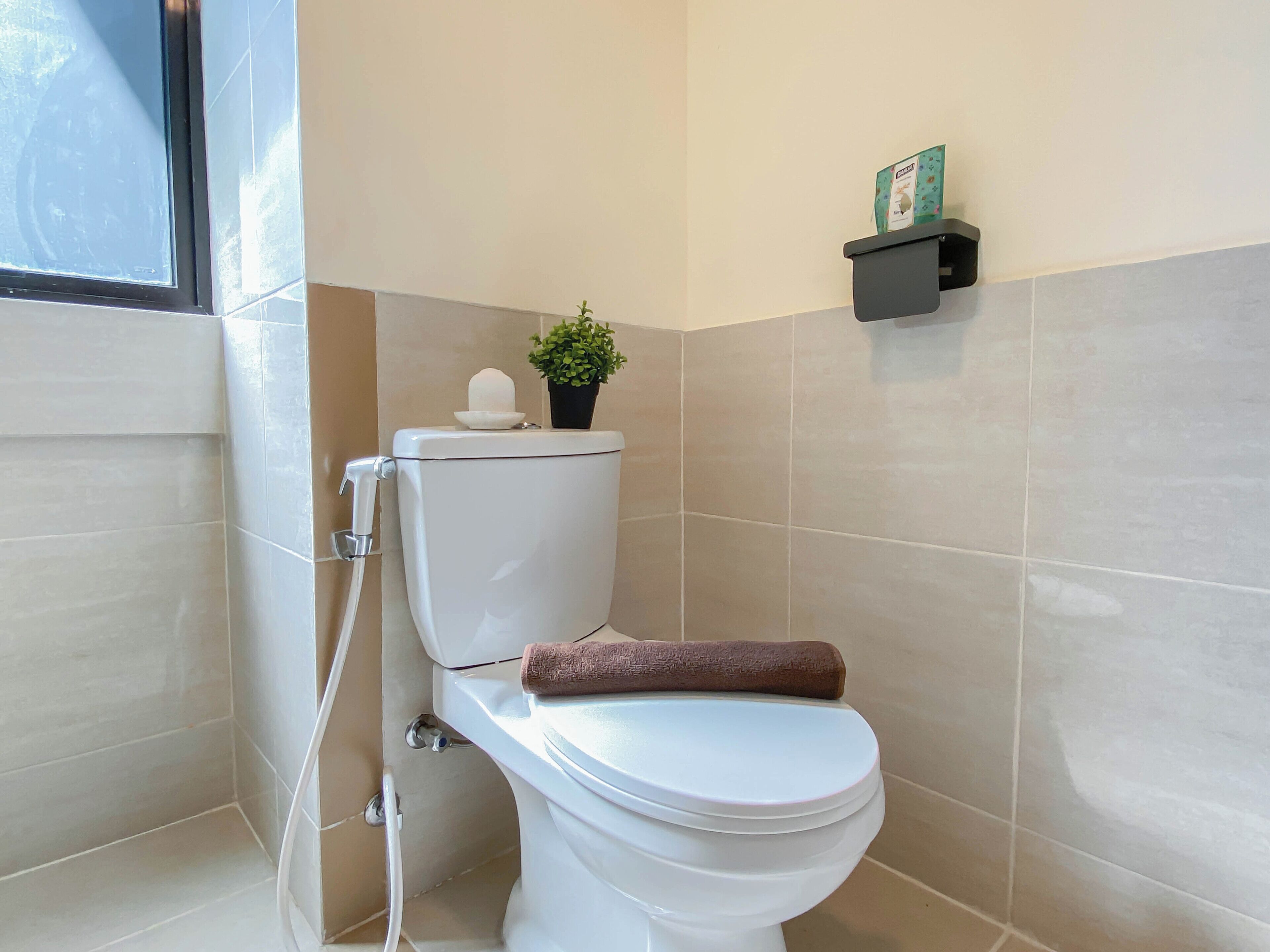 A bathroom with a toilet, a shower, and a shelf with a box.