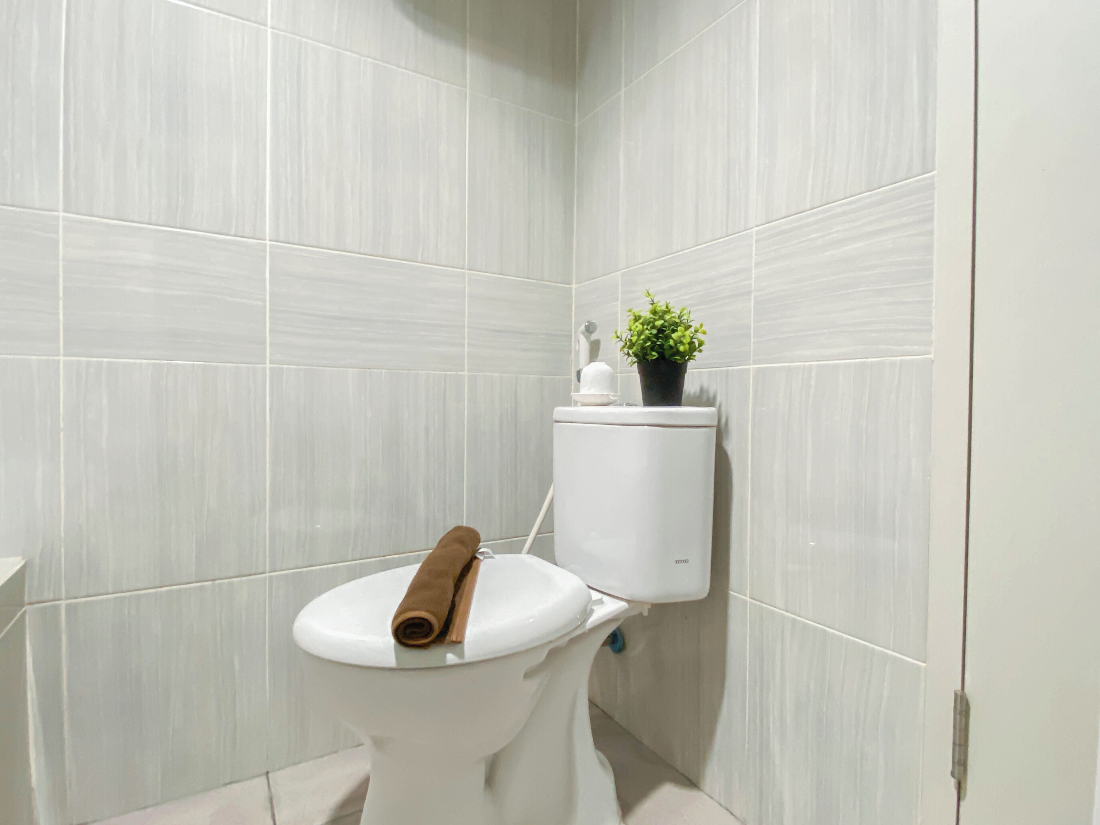 A modern bathroom with white tiled walls and a white toilet with a towel on the lid.