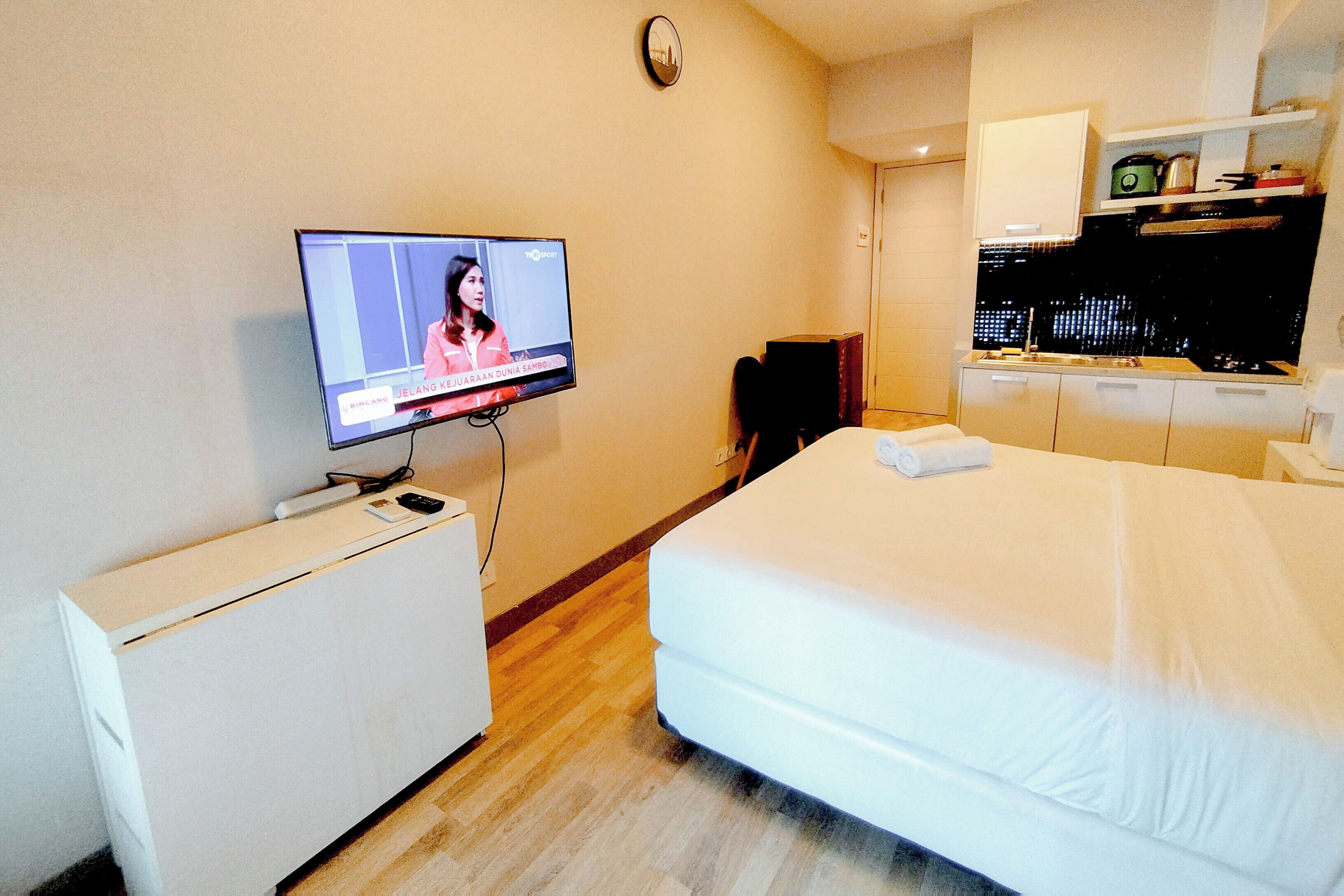 A hotel room with a bed, a TV, a desk, and a kitchenette.