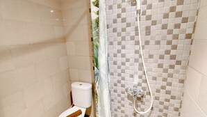 Un baño con inodoro, ducha y pared de azulejos a cuadros, además de una cortina.