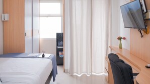 A hotel room with a bed, a desk, a TV, and a vending machine. - Warm And Cozy Studio Apartment At Serpong Garden (Cisauk)