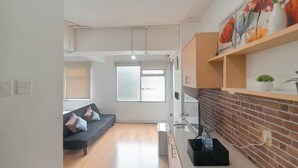Un salon moderne avec un canapé, un coin repas avec un mur en briques et une cuisine équipée d’un réfrigérateur.