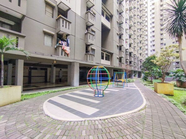 A residential building with multiple balconies, a playground with colorful spherical structures, and a paved courtyard. - Cozy Stay 3Br Apartment Gateway Ahmad Yani Cicadas (Bandung)