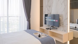 A modern hotel room with a large bed, a mounted TV displaying streaming services, and a marble wall. - Stunning Studio At Sky House Bsd Apartment (Pagedangan)