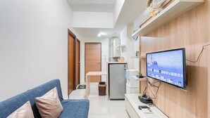 Una sala de estar moderna con un sofá, un televisor de pantalla plana montado en la pared, una mesita y un refrigerador.