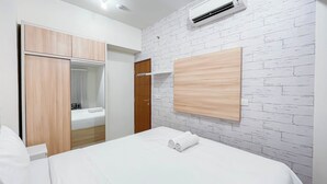 Una habitación de hotel con una cama, un armario de madera, un espejo y una pared de ladrillo blanco.