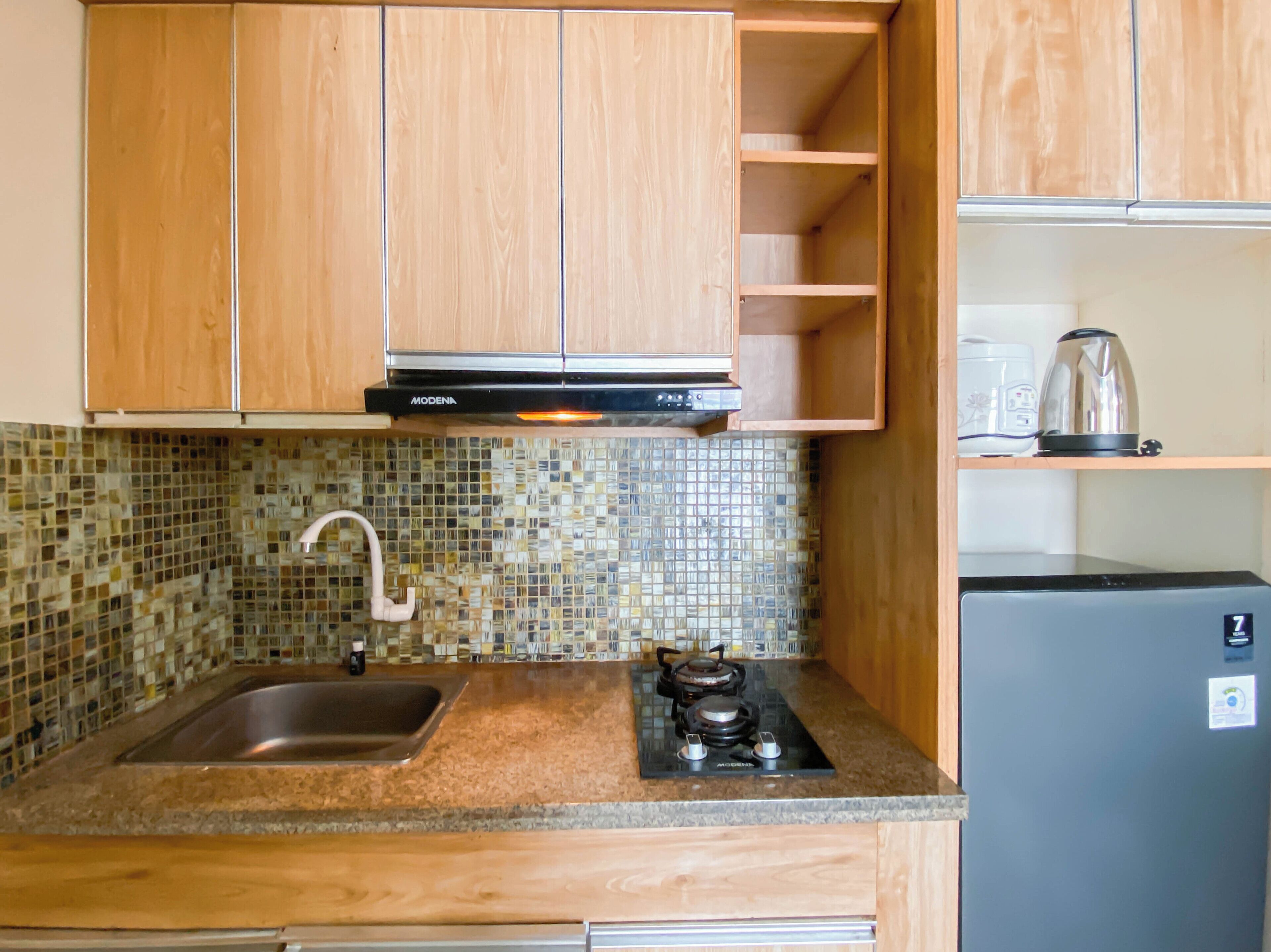 A kitchen with wooden cabinets, a tiled backsplash, a stainless steel sink, a gas stove, and a refrigerator.