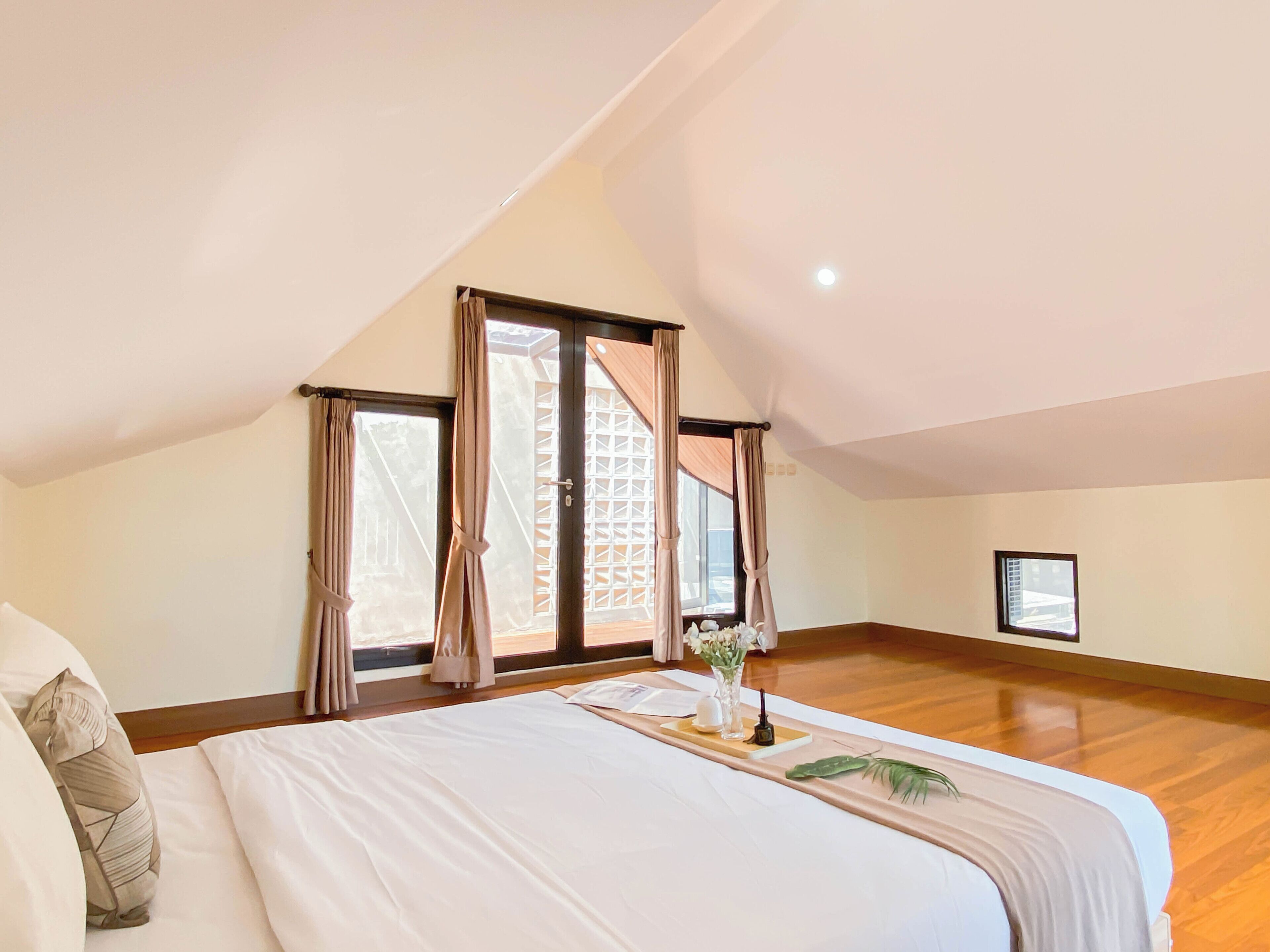 Un dormitorio con una cama grande, una ventana con cortinas y suelo de madera.