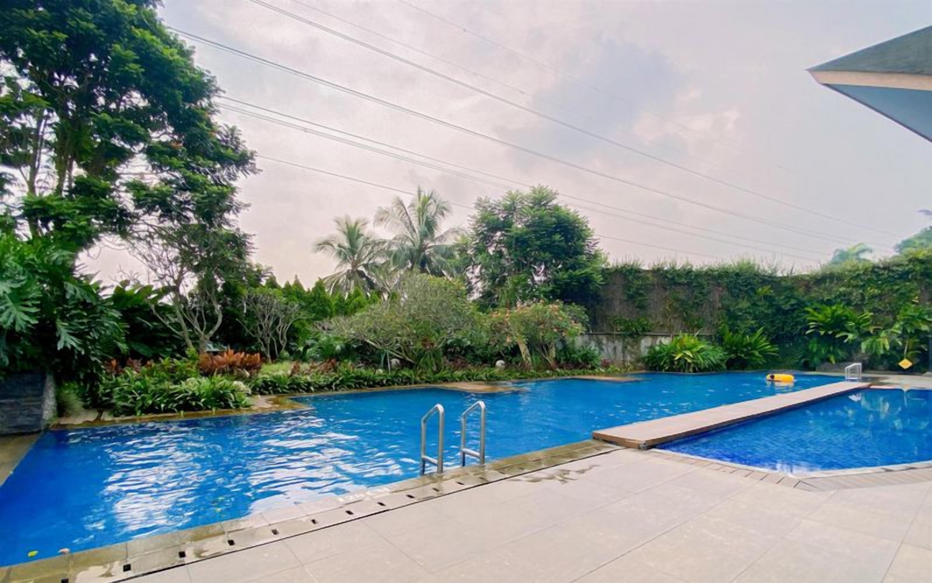 A swimming pool with a clear blue water, surrounded by lush greenery and a tiled deck.
