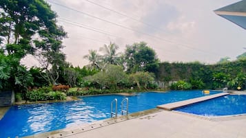 A swimming pool with a clear blue water, surrounded by lush greenery and a tiled deck.