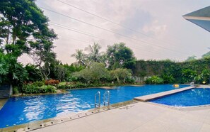 A swimming pool with a clear blue water, surrounded by lush greenery and a tiled deck. - Spacious And Comfy 3Br (6 Pax) At Vimala Hills Villa & Resort Gadog (Ciawi)