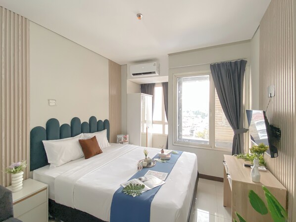 Hotellihuone, jossa on sänky, työpöytä, ilmastointilaite, ikkuna verhoilla ja näkymä ulos.