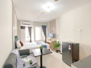 Hotellihuone, jossa on sänky, sohva, pieni pöytä, televisio ja jääkaappi.