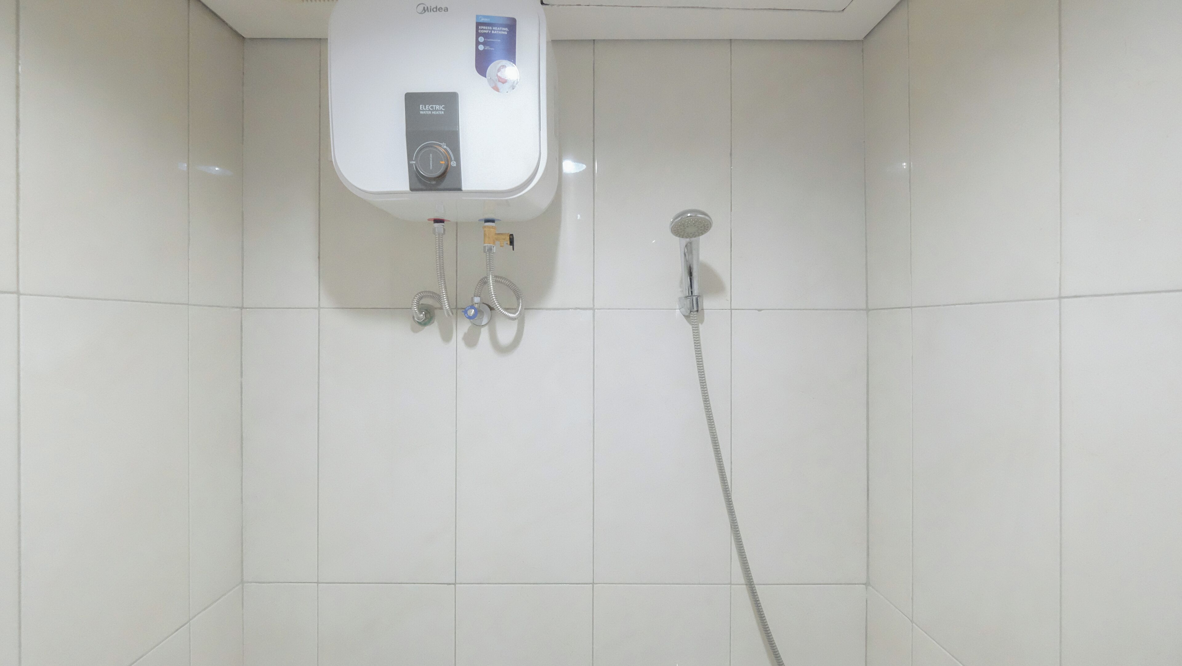 A bathroom with a white tiled wall, a water heater, and a shower.