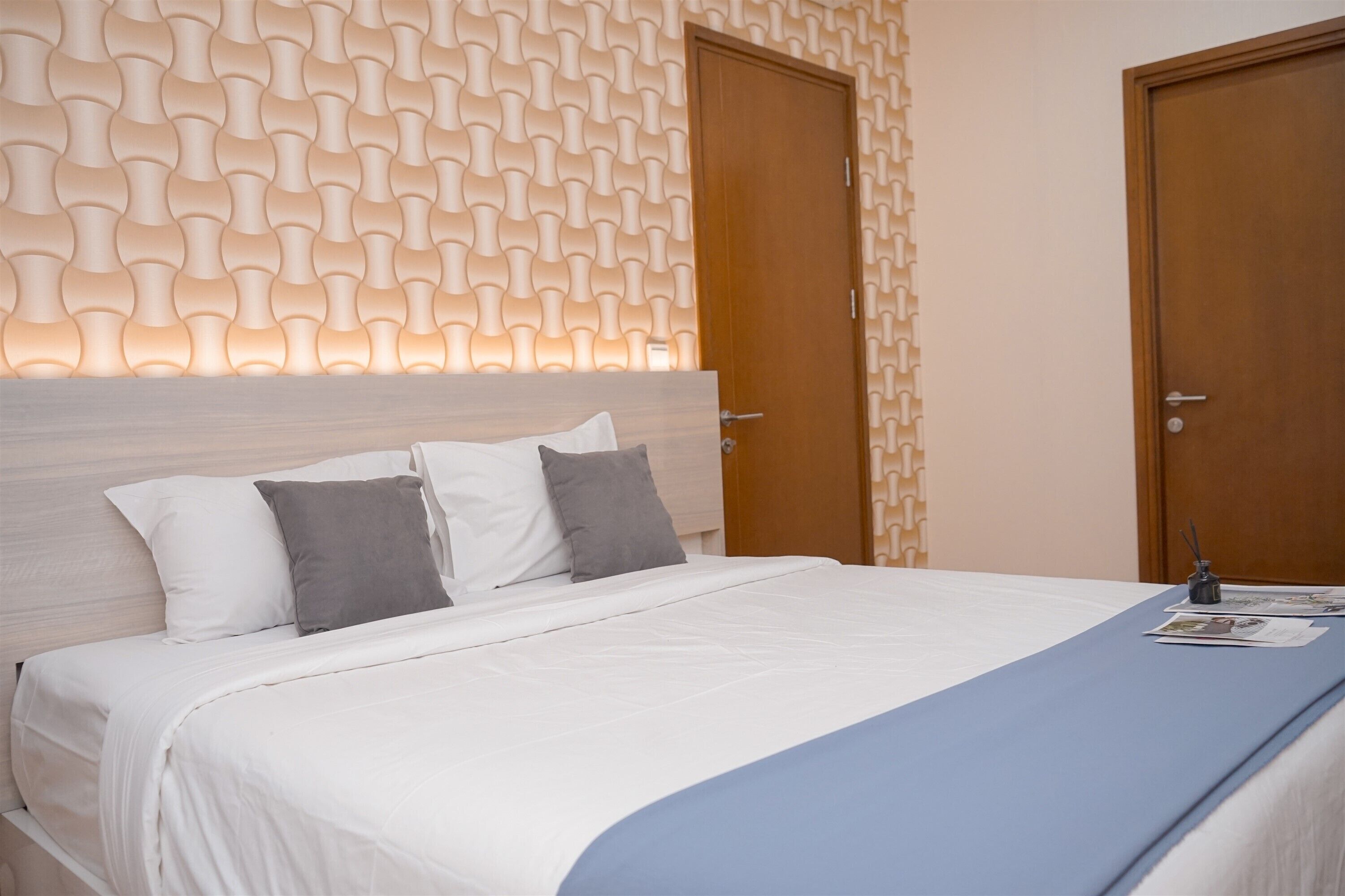 A neatly made bed with white and gray bedding, a wooden headboard, and a blue accent.