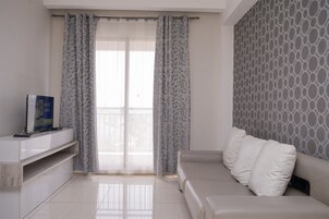 Una sala de estar moderna con un sofá, un televisor de pantalla plana y una ventana con cortinas estampadas.