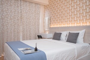 Una cama bien hecha con colcha azul, almohadas blancas y una mesita de noche con lámpara.