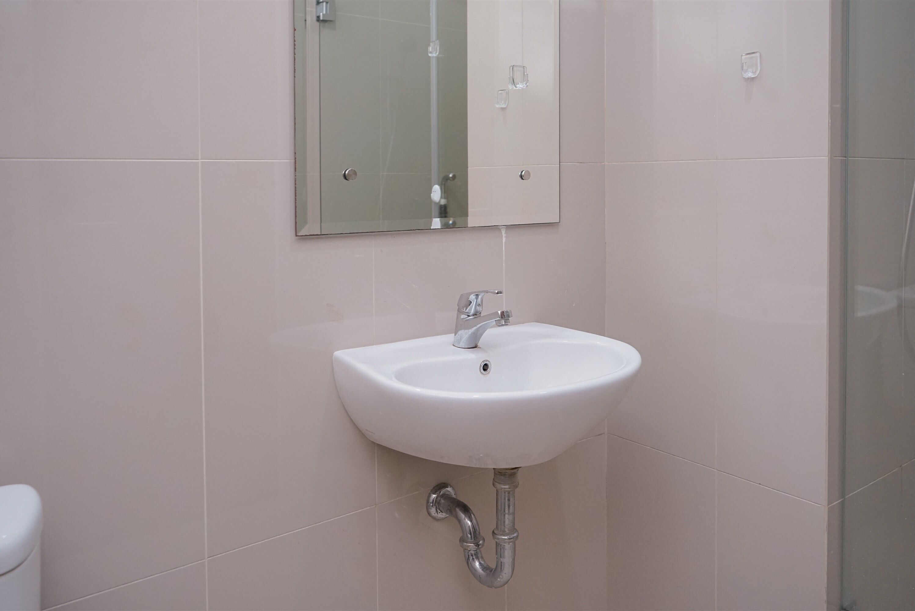 Un baño con un lavamanos blanco, un espejo encima y un inodoro a la izquierda.