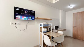 A modern kitchen with a TV mounted on the wall displaying a movie, a microwave, a sink, and a small dining area with chairs. - Comfortable Studio Room Apartment (No Kitchen) At Bandaraya Tallasa City Makassar (Makassar)