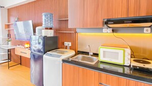 A modern kitchen with wooden cabinets, a built-in microwave, a coffee machine, and a water dispenser. - Spacious And Cozy Studio Apartment Vasanta Innopark (Cikarang)