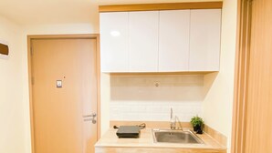 A compact kitchen with a wooden door, white cabinets, a sink, and a small potted plant. - Best Choice And Comfy 2Br At Apartment Meikarta (Cikarang)