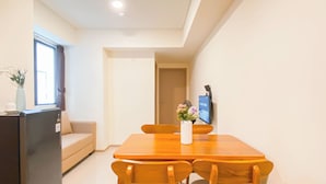A dining area with a wooden table and chairs, a small refrigerator, a sofa, and a TV on the wall. - Best Choice And Comfy 2Br At Apartment Meikarta (Cikarang)