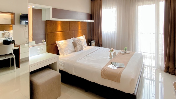 A hotel room with a large bed, a bedside table, a mirror, a TV, and a window with curtains.