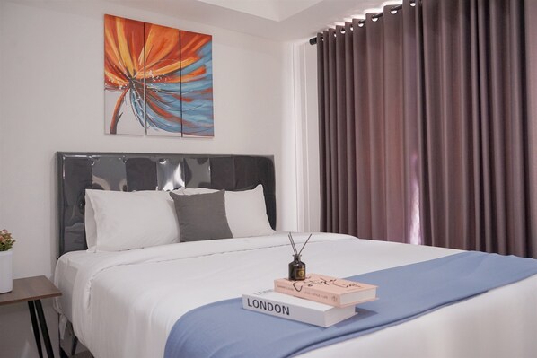 Quarto de hotel moderno com uma cama grande, cabeceira, mesa de cabeceira, pintura decorativa e uma janela com cortinas.
