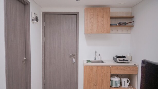 A compact kitchenette with a wooden cabinet, a sink, and a microwave. - Elegant And Homey 1Br Apartment Tamansari Bintaro Mansion (South Tangerang)