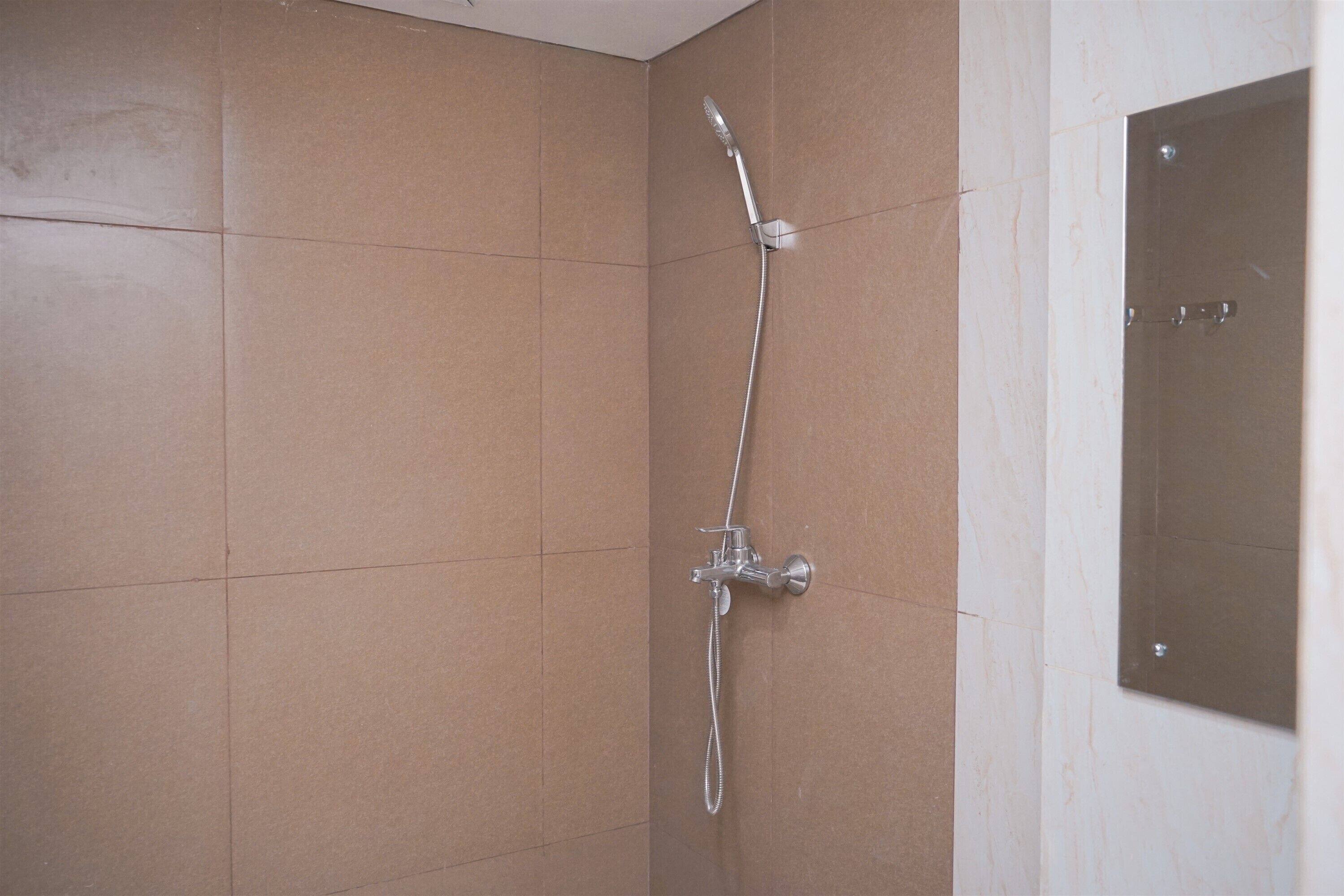 A shower with a handheld showerhead and a wall-mounted faucet in a tiled bathroom.