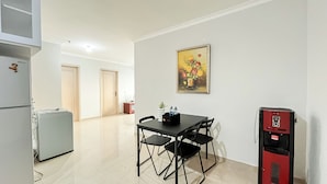 A compact kitchen with a refrigerator, a small table with chairs, a water dispenser, and a painting on the wall.