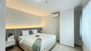 A modern hotel room with a bed, bedside table, lamp, and an air conditioning unit.