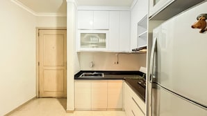 A compact kitchen with white cabinets, a black countertop, a stainless steel refrigerator, and a microwave.