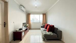 A living room with a sofa, a TV, a small table, and a window with curtains.